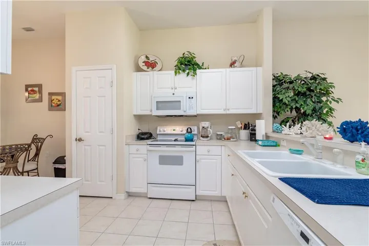 Kitchen with white appliances, white cabinetry, light tile patterned floors, and sink