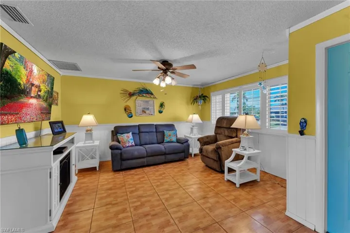Living room with crown molding, tile patterned floors, and ceiling fan