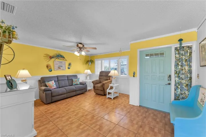 Tiled living room featuring ceiling fan, ornamental molding, and a textured ceiling