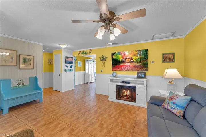 Living room with crown molding, ceiling fan, light tile patterned flooring, and a textured ceiling