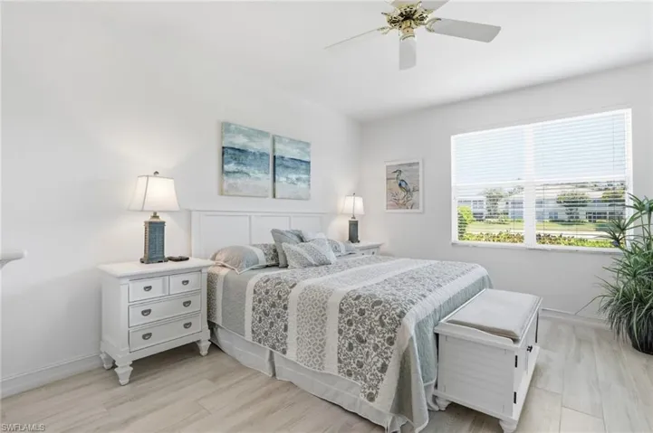 Bright bedroom featuring light wood-finish flooring, a ceiling fan, and a large window with horizontal blinds