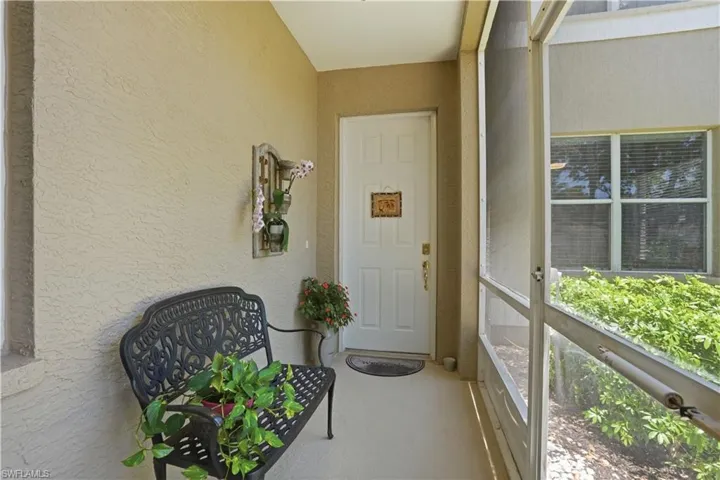 Screened entry porch featuring textured stucco walls, a paneled entry door, and concrete flooring
