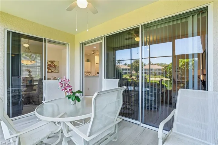 Screened lanai featuring textured walls, a ceiling fan, and multiple sliding glass doors with vertical blinds