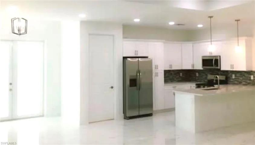 Kitchen featuring appliances with stainless steel finishes, tasteful backsplash, white cabinets, pendant lighting, and kitchen peninsula