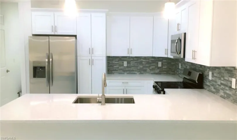 Kitchen featuring tasteful backsplash, white cabinets, sink, light stone countertops, and appliances with stainless steel finishes