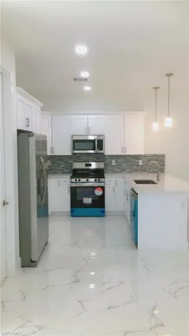 Kitchen side view featuring decorative light fixtures, light tile patterned flooring, decorative backsplash, sink, and appliances with stainless steel finishes