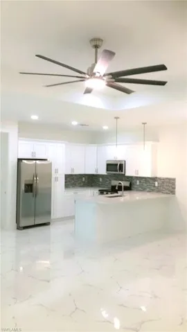 Kitchen featuring white cabinetry, decorative light fixtures, appliances with stainless steel finishes, light tile patterned floors, and backsplash