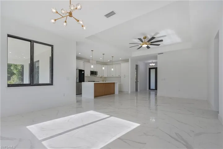 Unfurnished living room with light marble finish floors, a chandelier, a tray ceiling, a ceiling fan, and recessed lighting