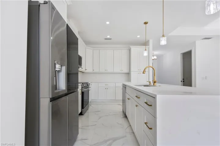 Kitchen with stainless steel appliances, a sink, light marble finish flooring, recessed lighting, and white cabinets