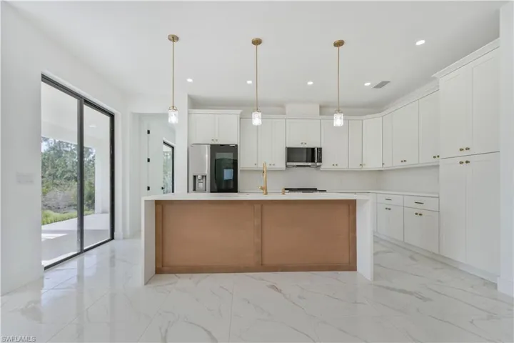 Kitchen featuring appliances with stainless steel finishes, white cabinetry, light marble finish floors, a center island with sink, and a sink