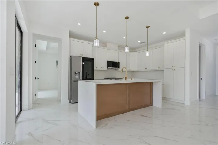 Kitchen with appliances with stainless steel finishes, white cabinetry, light marble finish flooring, an island with sink, and recessed lighting