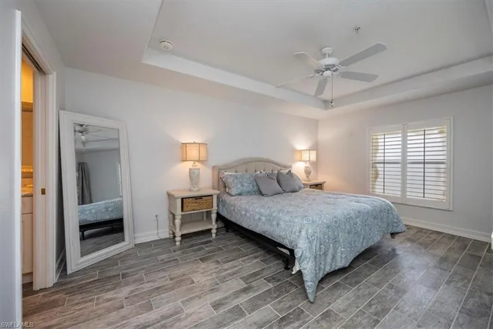 Bedroom featuring a raised ceiling, wood finished floors, baseboards, and ceiling fan