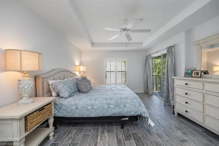 Bedroom featuring a tray ceiling, baseboards, access to outside, ceiling fan, and dark wood-type flooring