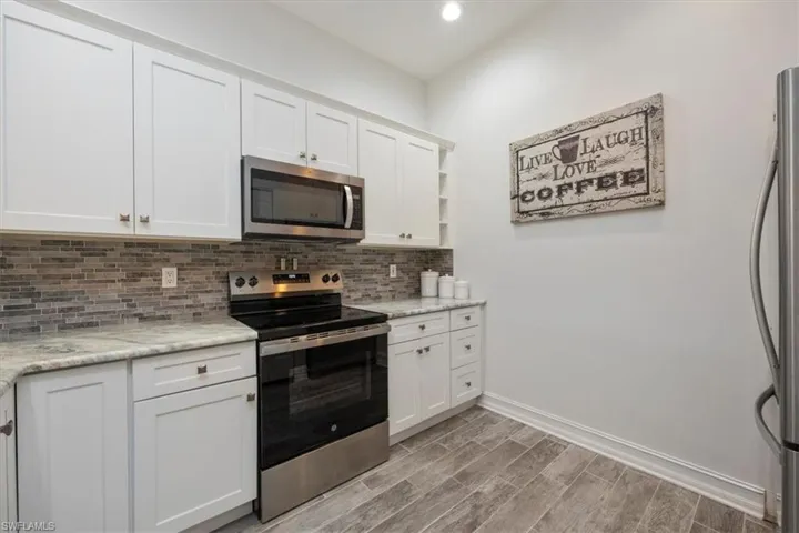 Kitchen with light wood-style floors, white cabinetry, backsplash, baseboards, and appliances with stainless steel finishes