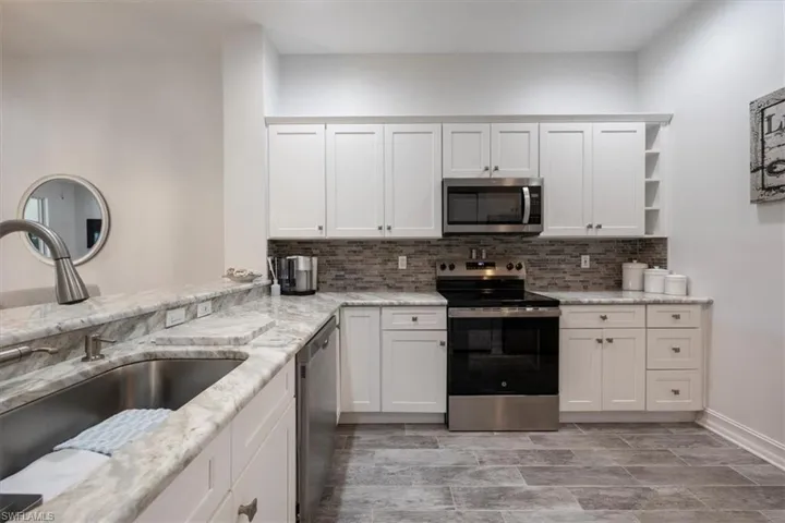 Kitchen with tasteful backsplash, white cabinetry, stainless steel appliances, and a sink