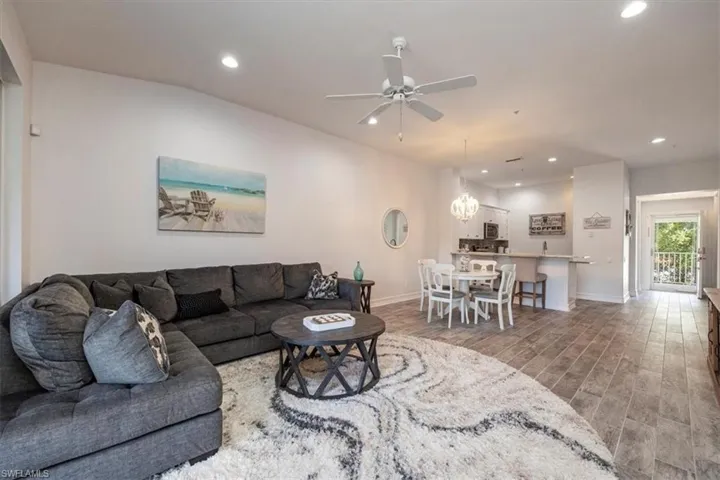 Living area with ceiling fan with notable chandelier, baseboards, wood finished floors, and recessed lighting