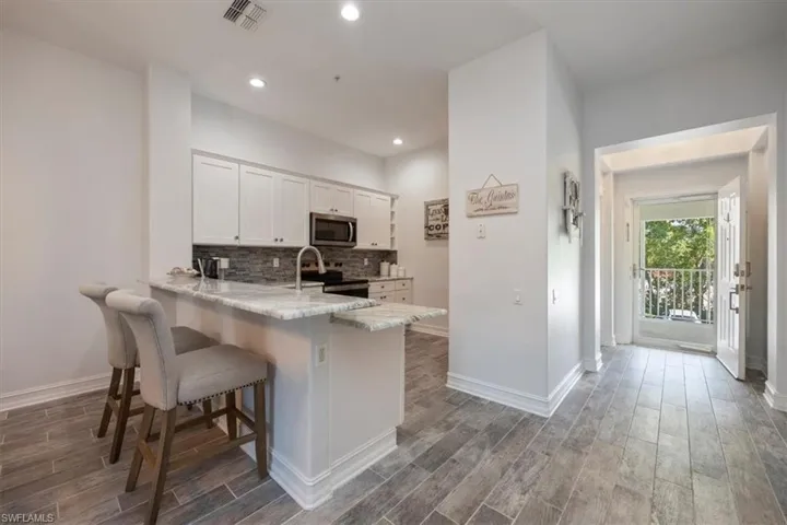 Kitchen featuring a kitchen breakfast bar, wood finished floors, appliances with stainless steel finishes, white cabinetry, and visible vents