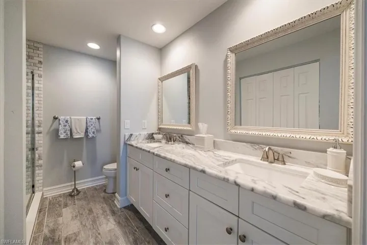 Full bathroom with toilet, a sink, double vanity, and baseboards