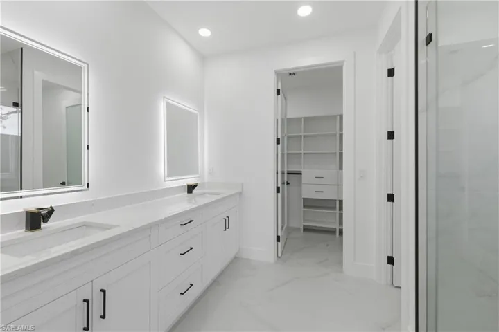 Bathroom featuring a spacious closet, double vanity, recessed lighting, a shower with shower door, and light marble finish floors
