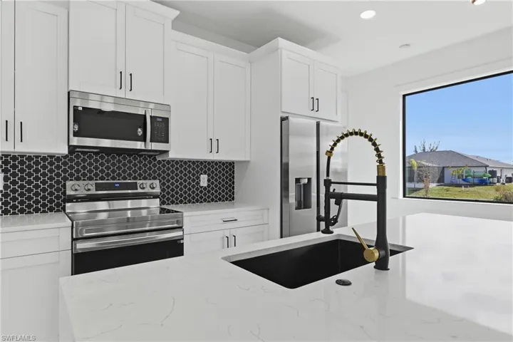 Kitchen with stainless steel appliances, white cabinetry, light stone countertops, backsplash, and recessed lighting