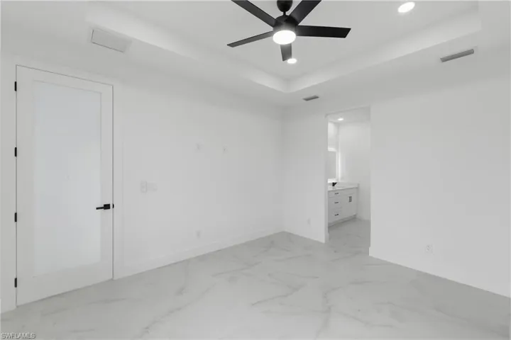 Unfurnished bedroom with a tray ceiling, recessed lighting, connected bathroom, ceiling fan, and light marble finish floors