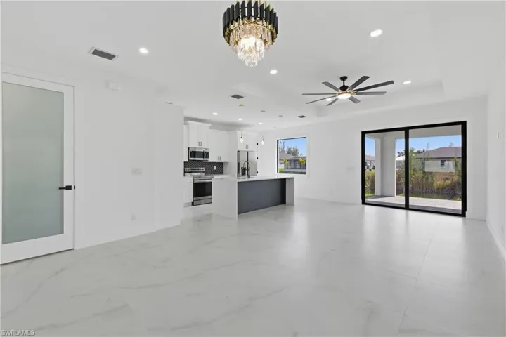 Unfurnished living room featuring a chandelier, a raised ceiling, recessed lighting, and a ceiling fan