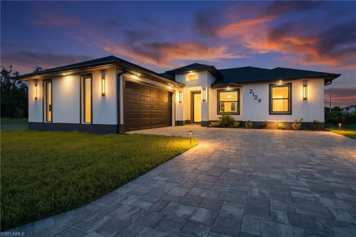 Prairie-style house featuring stucco siding, an attached garage, a front lawn, and decorative driveway