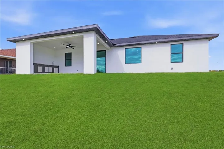 Back of house with a ceiling fan, a lawn, stucco siding, and a patio