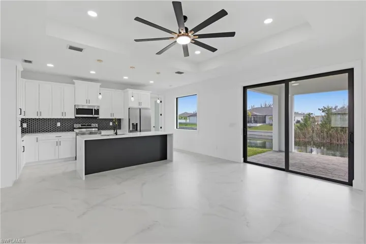 Kitchen featuring a tray ceiling, white cabinetry, an island with sink, stainless steel appliances, and a ceiling fan