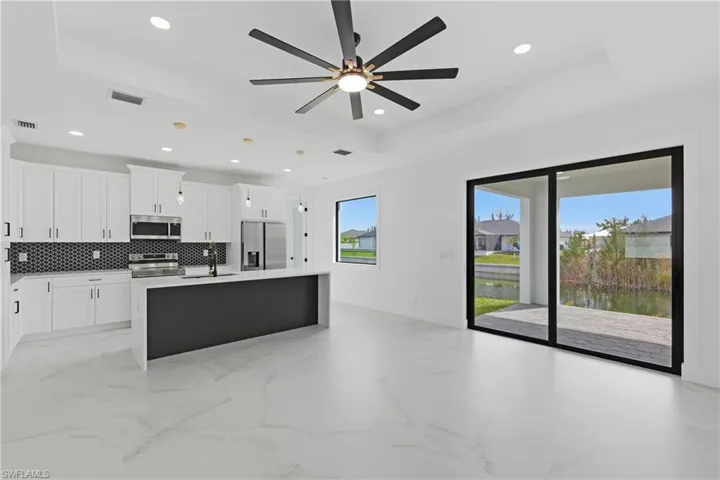 Kitchen featuring a tray ceiling, white cabinetry, an island with sink, stainless steel appliances, and light stone countertops
