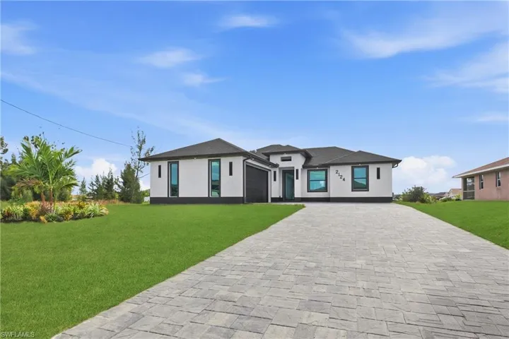 Prairie-style house featuring decorative driveway, a front lawn, stucco siding, an attached garage, and roof with shingles