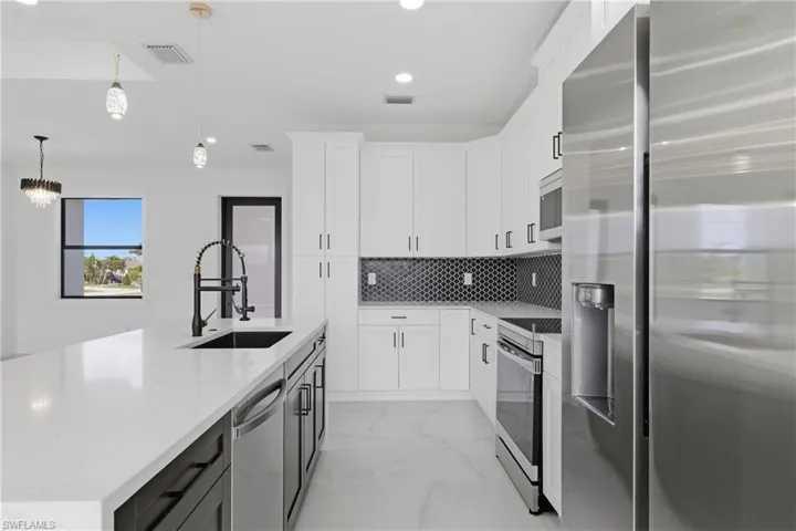 Kitchen featuring stainless steel appliances, white cabinets, light stone countertops, pendant lighting, and recessed lighting