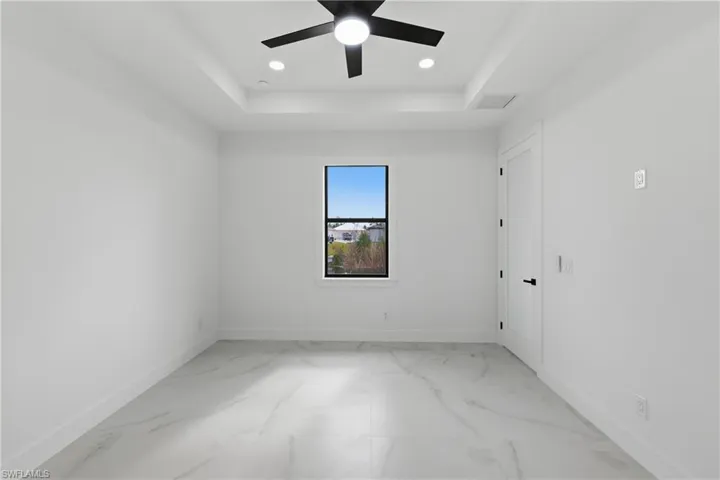 Unfurnished room with a raised ceiling, light marble finish flooring, recessed lighting, and a ceiling fan