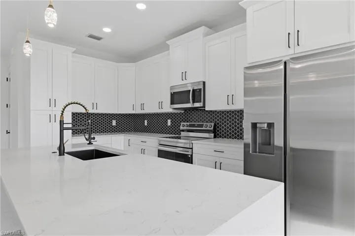 Kitchen featuring appliances with stainless steel finishes, light stone counters, a center island with sink, pendant lighting, and white cabinets