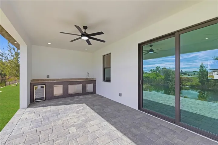 View of patio with beverage cooler, ceiling fan, exterior kitchen, and a water view