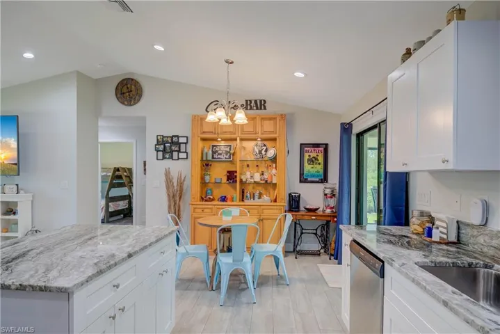 Kitchen with white cabinets, light stone counters, decorative light fixtures, lofted ceiling, and dishwasher