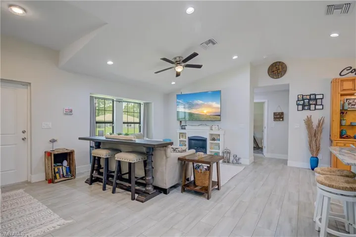 Living area with lofted ceiling, a glass covered fireplace, recessed lighting, wood finish floors, and ceiling fan