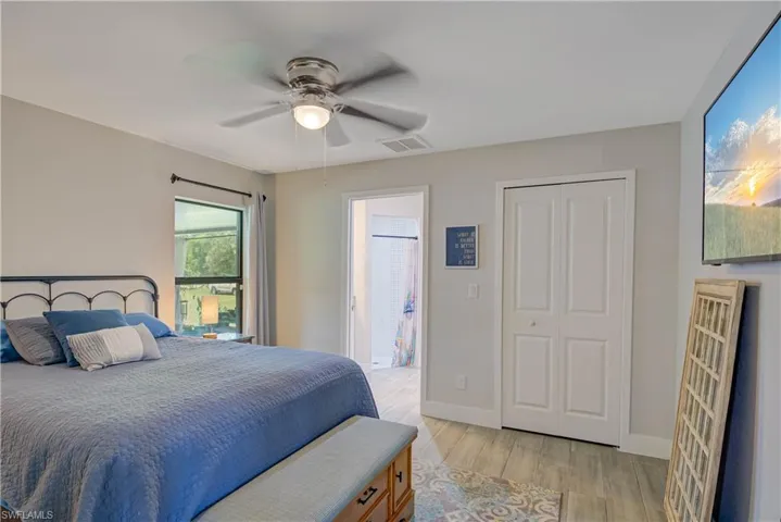 Bedroom with light wood-style floors, ceiling fan, ensuite bathroom, and a closet