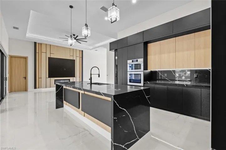 Kitchen with a tray ceiling, a sink, marble finish floor, modern cabinets, and dark cabinets
