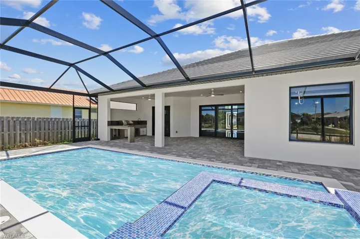 View of pool with glass enclosure, a patio area, exterior kitchen, and fence