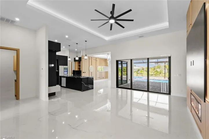 Living area featuring a tray ceiling, marble finish floor, visible vents, and a ceiling fan