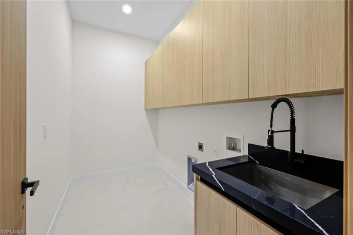 Clothes washing area featuring marble finish floor, washer hookup, a sink, cabinet space, and hookup for an electric dryer