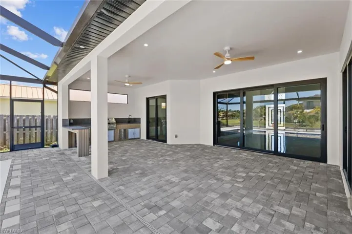 View of patio with ceiling fan, glass enclosure, an outdoor kitchen, and fence