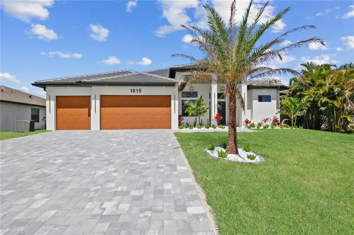 View of front facade with stucco siding, a front lawn, a garage, a tiled roof, and decorative driveway