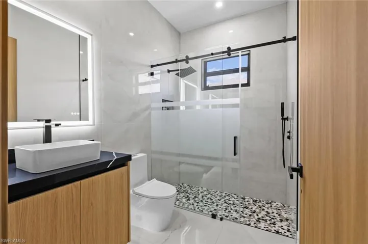 Bathroom with toilet, marble finish floor, a stall shower, and vanity