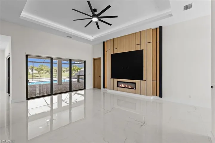 Unfurnished living room featuring visible vents, marble finish floor, a fireplace, a raised ceiling, and ceiling fan