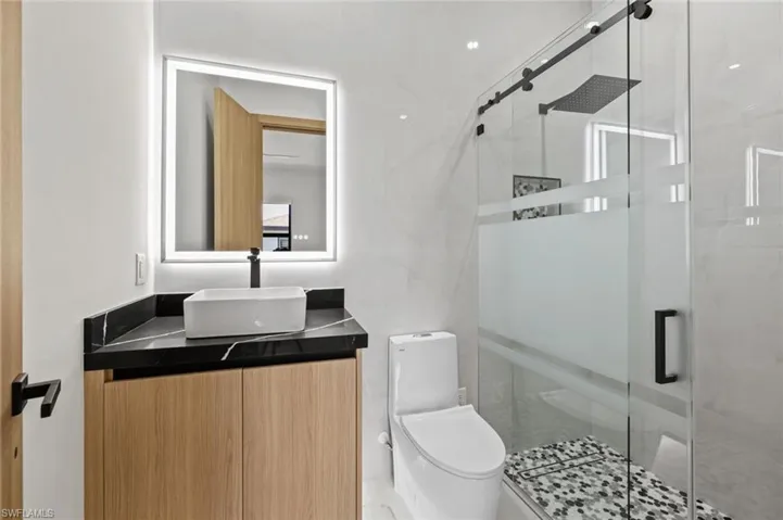 Bathroom with toilet, tile walls, a stall shower, and vanity