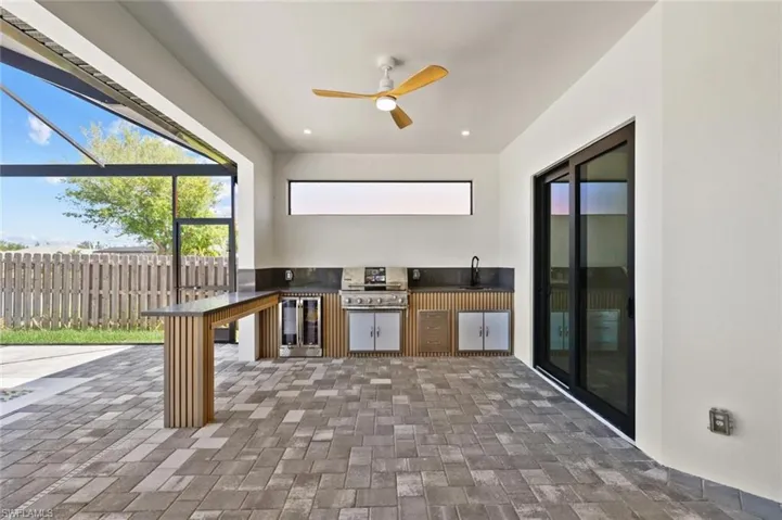 View of patio / terrace with grilling area, ceiling fan, fence, a lanai, and exterior kitchen