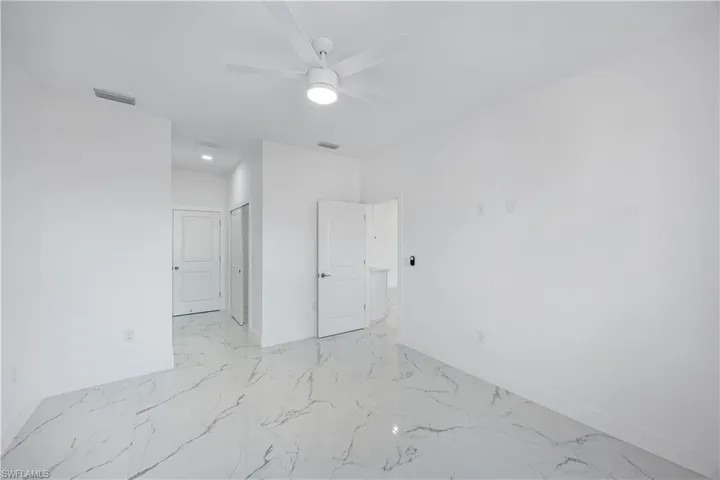 Primary bedroom with ceiling fan, light marble finish tile, and two walk in closets