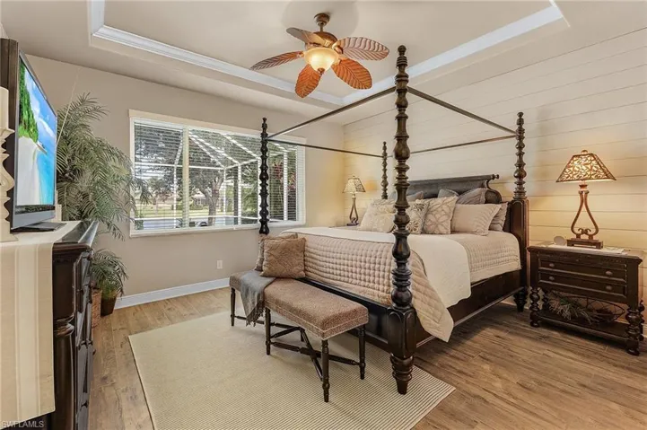 Primary bedroom with ensuite bathroom, tray ceiling with crown molding, and shiplap accent wall. Offers views of the lake and pool.